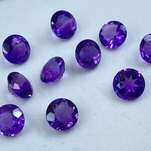 May include: Ten round, faceted amethyst gemstones in various shades of purple. The gemstones are approximately 6mm in diameter and have a smooth, polished finish.