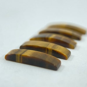 May include: Five tiger's eye stones, each with a curved, polished shape, arranged in a row on a white surface.