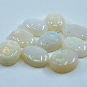 May include: A collection of nine white oval opal gemstones with iridescent flashes of color.