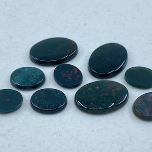 May include: A collection of nine oval-shaped, polished, green and red gemstone cabochons. The stones have a dark green base with red and orange inclusions.