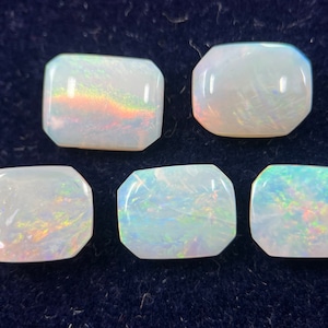 May include: Five white opal gemstones with iridescent rainbow colors. The gemstones are rectangular and have a smooth, polished finish.