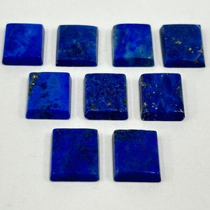 Könnte beinhalten: Zehn rechteckige Lapislazuli-Cabochons, jeder mit einer tiefblauen Farbe und goldenen Pyrit-Flocken. Die Steine sind glatt und poliert und in zwei Reihen auf einem weißen Hintergrund angeordnet.