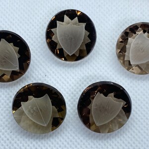 May include: Five round, brown, faceted, gemstone buttons with a carved, white, shield design.