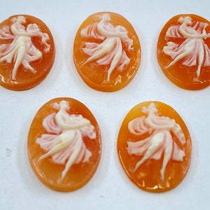 Könnte beinhalten: Fünf ovale Kameen-Anhänger mit einem geschnitzten Design von zwei tanzenden Figuren. Die Figuren sind in Weiß vor einem pfirsichfarbenen Hintergrund geschnitzt.
