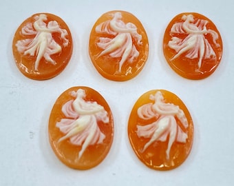 May include: Five oval-shaped cameo pendants with a carved design of two figures dancing. The figures are carved in white against a peach-colored background.