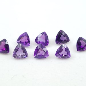 May include: Eight triangular amethyst gemstones, each with a purple hue, are arranged in a row on a white surface.