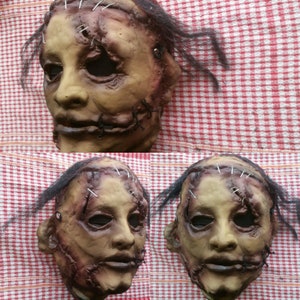 May include: A close-up of a realistic horror mask with stitched-up skin and a sewn-shut mouth. The mask is made of a flesh-toned material and has a realistic texture. The mask is shown from three different angles.