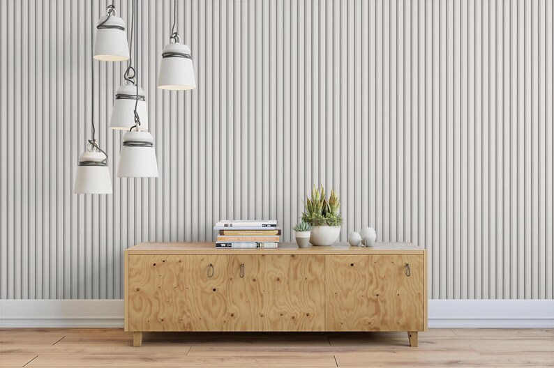a wooden cabinet with a stack of books on top, a potted plant, and a small white bowl on the surface. The cabinet is situated against a striped wall, and there are six white pendant lights hanging from the ceiling above it.