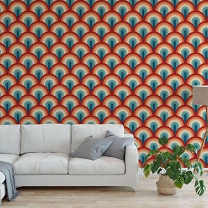a living room with a white sofa and a potted plant. The sofa is positioned against a wall with a vibrant, repeating pattern of colorful circles in shades of red, orange, yellow, green, blue, and purple. The potted plant is placed on the floor next to the sofa, adding a touch of greenery to the space.