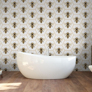 May include: A white bathroom with a bathtub and a toilet. The walls are covered in wallpaper featuring a pattern of bees in hexagonal cells. The wallpaper is white with gold accents.