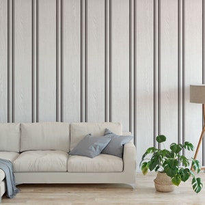 May include: A white sectional sofa with grey throw pillows sits in front of a wall with vertical wood panelling. A green plant in a brown pot and a wooden floor lamp with a beige lampshade are on the floor.