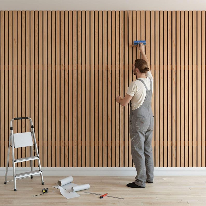 A man is working on a wall, using a tool to apply paint or wallpaper to it. There is a ladder and some tools on the floor nearby, indicating that the room is in the process of being renovated or decorated.