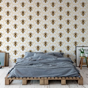 May include: A bedroom featuring a bed and a white wall adorned with a repeating pattern of yellow and brown bees in hexagonal shapes. A small potted plant sits on a wooden stool, and a framed print hangs on the wall.