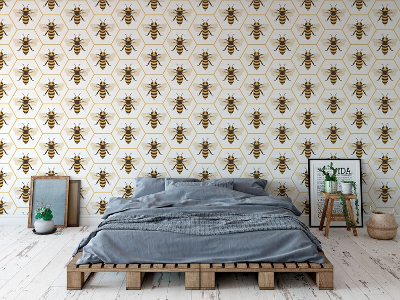 May include: A bedroom featuring a bed and a white wall adorned with a repeating pattern of yellow and brown bees in hexagonal shapes. A small potted plant sits on a wooden stool, and a framed print hangs on the wall.