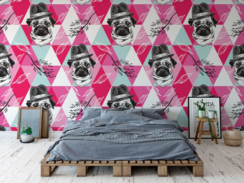 Puede incluir: Un dormitorio con un papel tapiz de patr&oacute;n geom&eacute;trico rosa, azul y blanco con un dise&ntilde;o repetido de un pug con sombrero. El papel tapiz est&aacute; detr&aacute;s de una cama con un edred&oacute;n gris y un marco de madera.