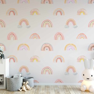 Puede incluir: Una habitaci&oacute;n de beb&eacute; con una pared blanca con un patr&oacute;n repetitivo de arco&iacute;ris coloridos. La habitaci&oacute;n tiene una c&oacute;moda blanca, dos cestas de almacenamiento grises y dos l&aacute;mparas de noche de conejo blanco.
