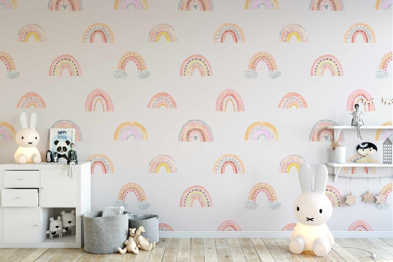 Puede incluir: Una habitaci&oacute;n de beb&eacute; con una pared blanca con un patr&oacute;n repetitivo de arco&iacute;ris coloridos. La habitaci&oacute;n tiene una c&oacute;moda blanca, dos cestas de almacenamiento grises y dos l&aacute;mparas de noche de conejo blanco.