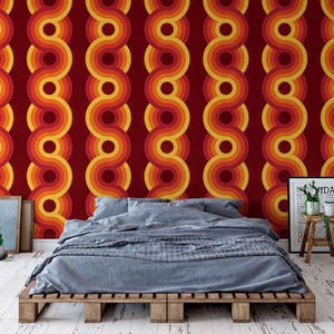 a bedroom with a bed, a wooden pallet table, and a framed poster on the wall. The wall has a vibrant, retro-style wallpaper with a repeating pattern of circles in shades of red, orange, and yellow.