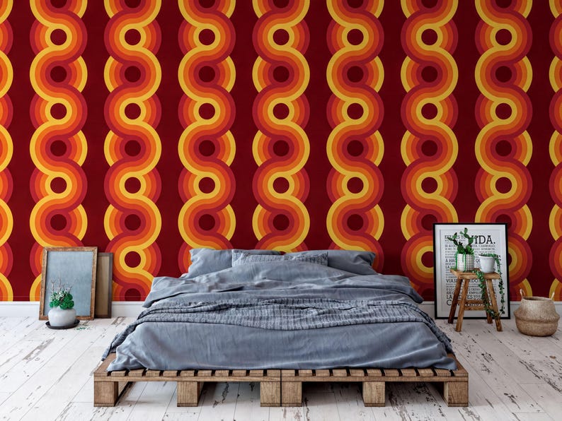 a bedroom with a bed, a wooden pallet table, and a framed poster on the wall. The wall has a vibrant, retro-style wallpaper with a repeating pattern of circles in shades of red, orange, and yellow.