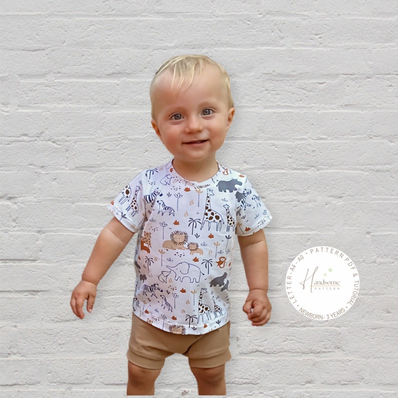May include: A toddler wearing a white short-sleeved t-shirt with a brown, black, and white animal print. The shirt has a round neckline and short sleeves. The toddler is also wearing brown shorts. The image includes a logo for "Handsome Pattern" with the text "Letter A4 AOPattern PDF & Tutorial Newborn - 3 Years".