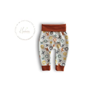 Op de afbeelding: Babybroek van lichtgrijze gem&ecirc;leerde stof met een herhalend patroon van handgetekende X- en O-symbolen in mosterdgeel, roestoranje en leiblauw. De broek heeft een effen roestoranje tailleband en boorden bij de enkels.