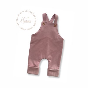 May include: A dusky pink baby's overall with wooden buttons and ribbed cuffs. The straps cross at the back. The image includes the text "Handsome Pattern" and "1 month - 6 years".