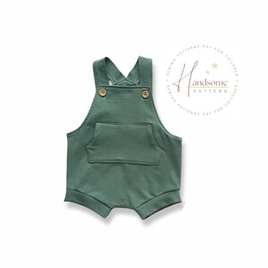 May include: A green romper with a front pocket and wooden buttons. The straps cross at the back. The romper is designed for children. The text "Handsome Pattern" is in a circle on the right side.
