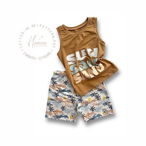 May include: A tan tank top and matching shorts set. The tank top features the text "SURF SAND" with palm tree graphics. The shorts have a tropical print with palm trees, mountains, and a sunset. The set is designed for children.
