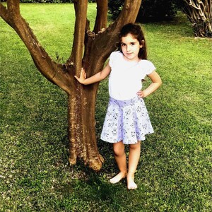 May include: A white short-sleeved top with ruffled sleeves paired with a light purple skirt featuring a repeating black and white pattern of small animal illustrations. The skirt has a wide waistband and a flared silhouette that reaches above the knees.