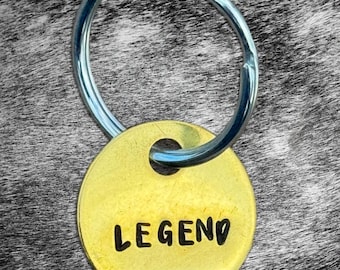May include: A gold-coloured key chain with a silver ring and a round tag that says "LEGEND" in black lettering.