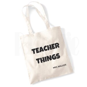 May include: A white canvas tote bag with black text that reads "TEACHER THINGS" and "MRS WALKER".