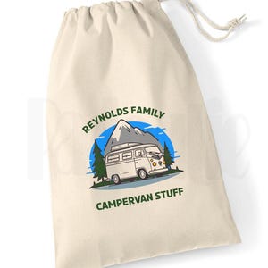 May include: A white canvas tote bag featuring a green and blue graphic of a camper van in front of a mountain. The text "Reynolds Family Campervan Stuff" is printed on the bag.