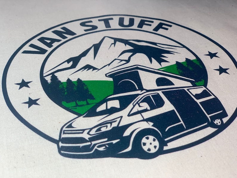 May include: A white canvas tote bag with a blue and green logo. The logo features a mountain range, trees, a camper van, and the text "VAN STUFF".
