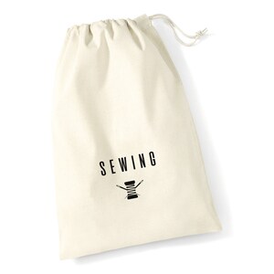 May include: A white cotton drawstring bag with the word "SEWING" printed in black letters and a black silhouette of a spool of thread with two needles.