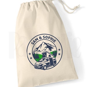 May include: A white canvas drawstring bag with a blue and green logo featuring a mountain, trees, and a camper van. The logo also includes the text "SAM & SOPHIE" in a circle.
