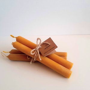Könnte beinhalten: Ein Bündel aus sechs dünnen, gelben Bienenwachskerzen, die mit Schnur zusammengebunden sind und ein braunes Papieretikett mit der Aufschrift "Honey 100% Pure Beeswax" tragen.