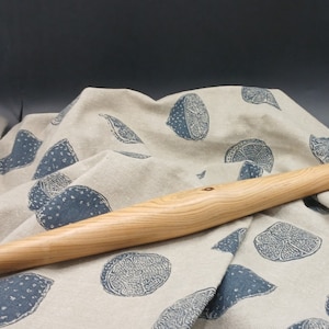 Può includere: Un mattarello di legno con finitura naturale, appoggiato su un tessuto di lino beige con stampa di limone blu.