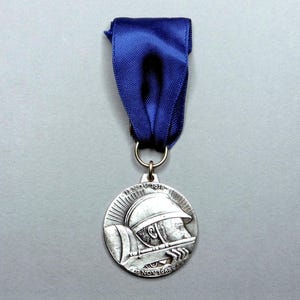 May include: A silver medal with a blue ribbon. The medal features a soldier in a helmet and the dates 11 NOV 1918 and 11 NOV 1668. The ribbon is a deep blue color.