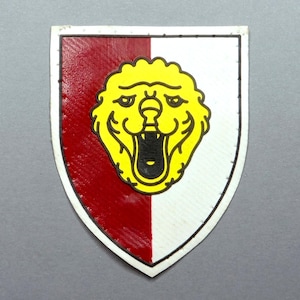 May include: A shield-shaped emblem with a red and white split background. A yellow lion's head with an open mouth is centered on the shield. The emblem has a silver border.
