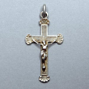 Peut inclure: Pendentif crucifix argenté représentant Jésus-Christ. La croix présente des ornements décoratifs aux extrémités des bras et à la base, avec une boucle pour une chaîne en haut. La figure du Christ est d'une couleur contrastée.