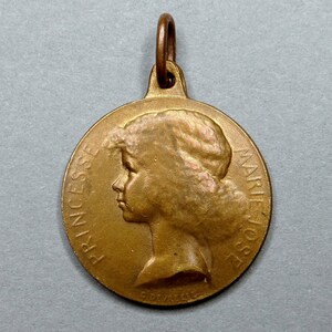 Puede incluir: Una medalla de bronce con un perfil de una joven en un lado. La inscripción "PRINCESSE MARIE JOSE" está alrededor del borde de la medalla.