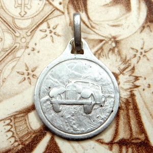 Peut inclure: Breloque en argent représentant une voiture ancienne en relief. Le breloque est rond et possède une boucle en haut pour l'attacher à un collier ou un bracelet.