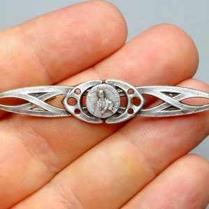 May include: Silver-toned brooch with a Celtic knot design and a circular medallion featuring a religious figure. The medallion has the text "St. Jude Thaddeus" around the edge.