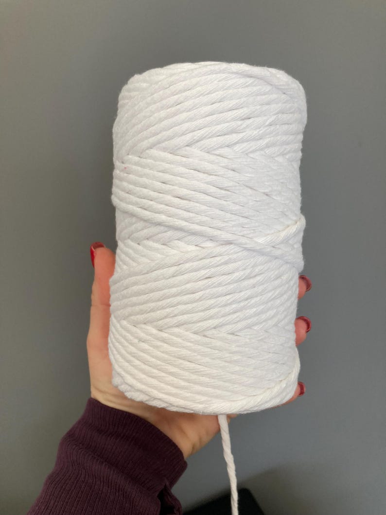 K&ouml;nnte beinhalten: Ein wei&szlig;es Baumwollseil, zu einer Spule gewickelt, wird in einer Hand gehalten. Das Seil ist dick und hat eine nat&uuml;rliche Textur.
