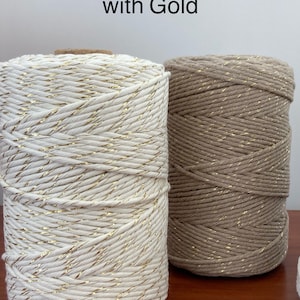 May include: Two spools of cotton rope with gold thread running through it. The spool on the left is ecru and the spool on the right is beige. The text "Ecru with Gold" and "Beige" is written above the spools.