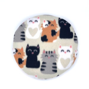 Pode incluir: Almofada redonda creme com um padrão repetido de gatos de desenho animado. Os gatos são pretos, cinzentos, laranja e brancos, cada um com um rosto sorridente e detalhes em forma de coração. Um item com tema de gato.