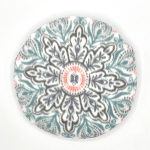 Op de afbeelding: Een rond, wit, pluche kussen met een teal, grijs en roze mandala-ontwerp.