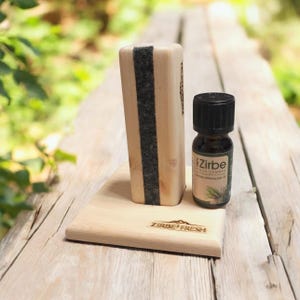 Könnte beinhalten: Ein hölzernes Aromatherapie-Diffusor-Set mit einer kleinen ätherischen Ölflasche. Der Diffusor hat eine rechteckige Form mit einem dunkelgrauen Filzstreifen. Die ätherische Ölflasche hat einen schwarzen Deckel und ein Etikett mit der Aufschrift "Zirbe". Die Basis ist mit "Zirbe Fresh" graviert.