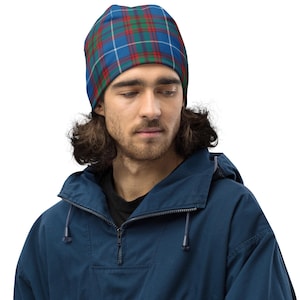 Könnte beinhalten: Ein blau, rot und grün kariertes Beanie. Die Person trägt eine marineblaue Kapuzenjacke. Das Beanie zeigt ein klassisches Tartanmuster und bietet ein stilvolles und warmes Accessoire.
