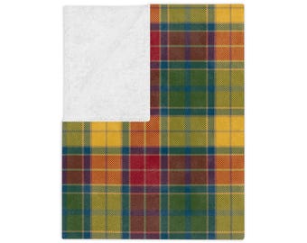 Pode incluir: Um cobertor dobrado com um padrão xadrez colorido. O design xadrez apresenta uma mistura de quadrados amarelos, verdes, vermelhos e azuis. O canto superior esquerdo do cobertor está dobrado, revelando um tecido branco e macio.
